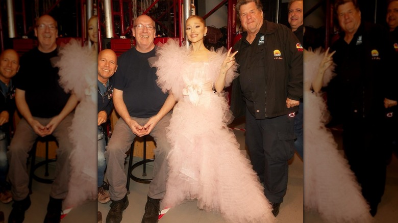 Ariana Grande poses backstage with crew members in a flouncy pink gown.