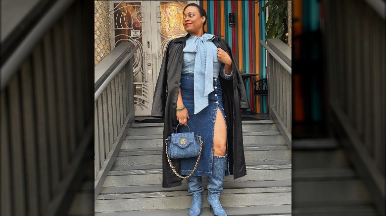 A woman wearing a denim skirt, boots, and bag