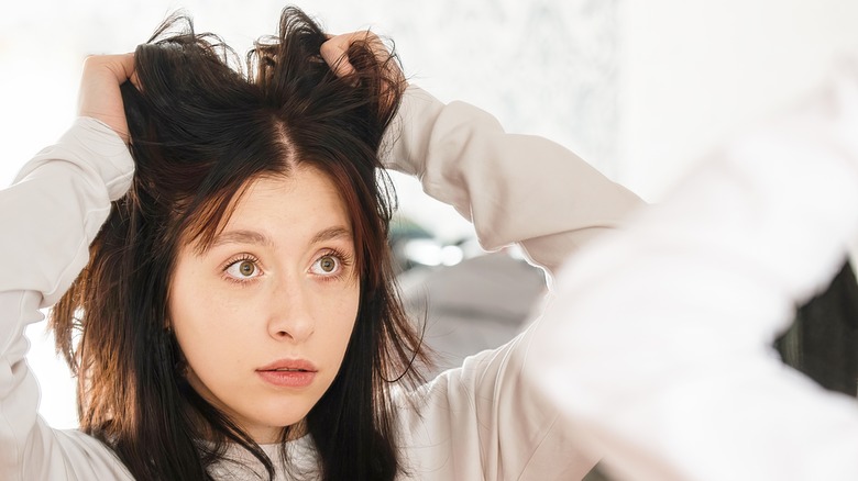 Woman analysing greasy hair in mirror 
