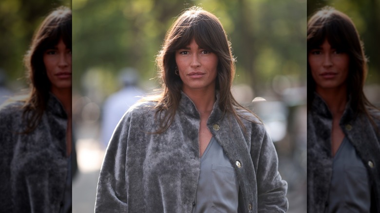 A woman with curtain bangs walking down the street looking at the camera.