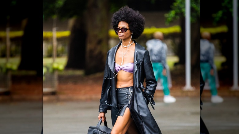 A woman with natural hair walking down the street wearing sunglasses and a leather coat.