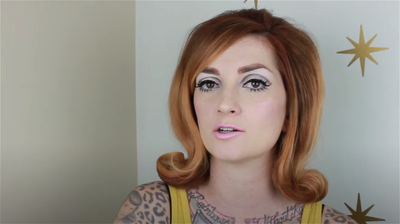 A woman with retro flipped hair and '60s makeup looks at the camera.