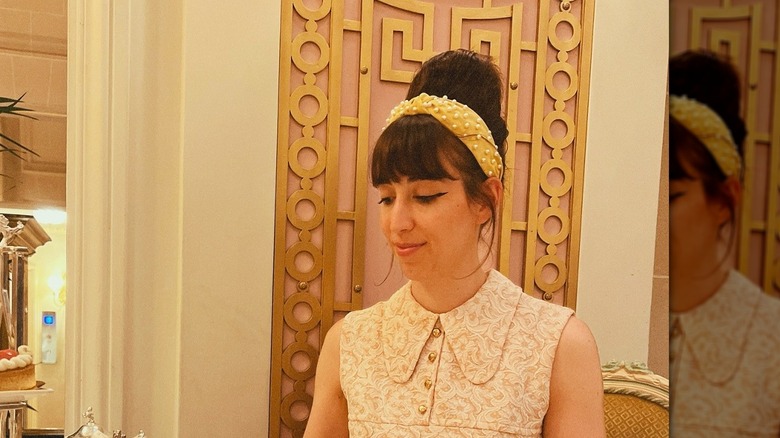 A woman with headband in her retro hair, wearing a collared sleeveless shirt.