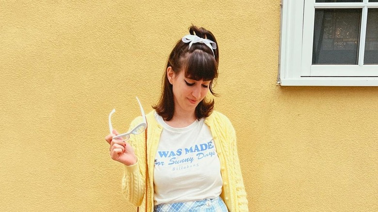 A woman wearing a white bow in her hair against a yellow wall.