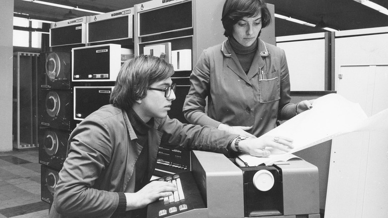 Two people using a computer from the '70s