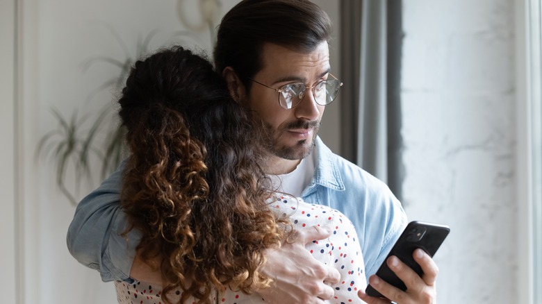 Couple hugging while man checks phone