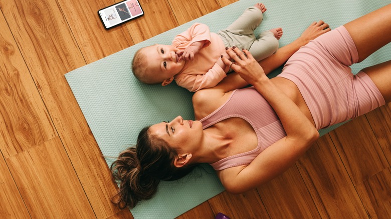 Woman lying on yoga mat with baby