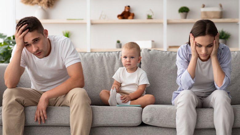 Upset couple on opposite ends of a couch with sad toddler in the middle