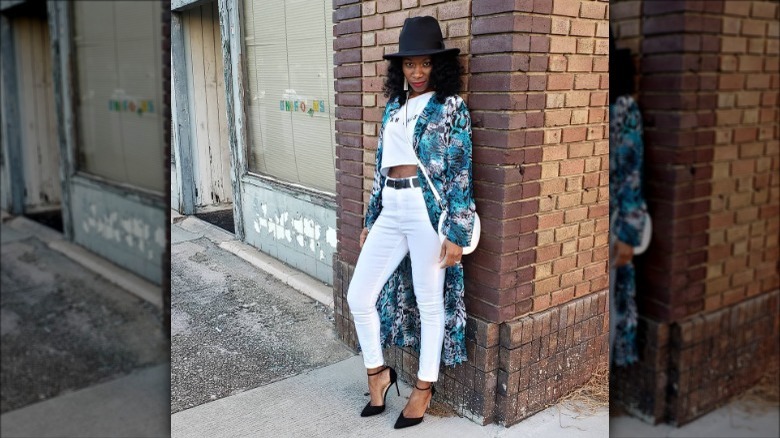 woman wearing patterned duster leaning against brick wall