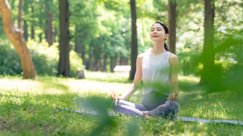 woman meditating in grass surrounded by trees