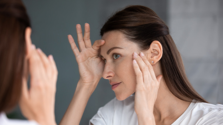 woman examining skin in mirror