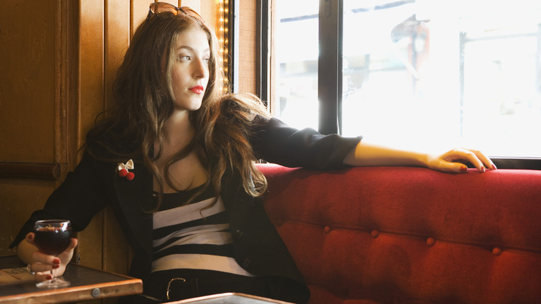 woman in booth looking out window holding glass of wine