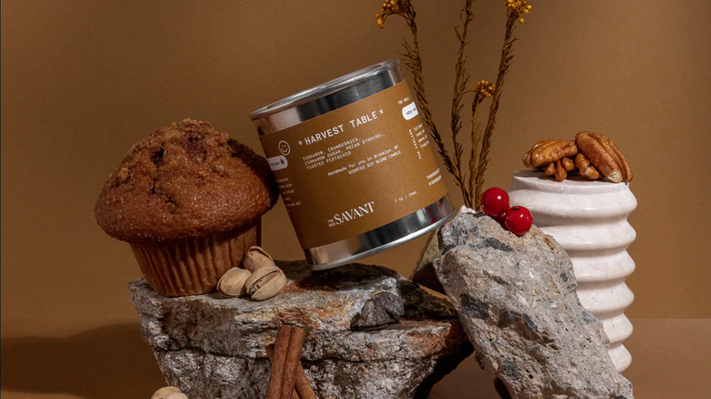 khaki colored candle tin atop rocks, pecans, muffins, and berries