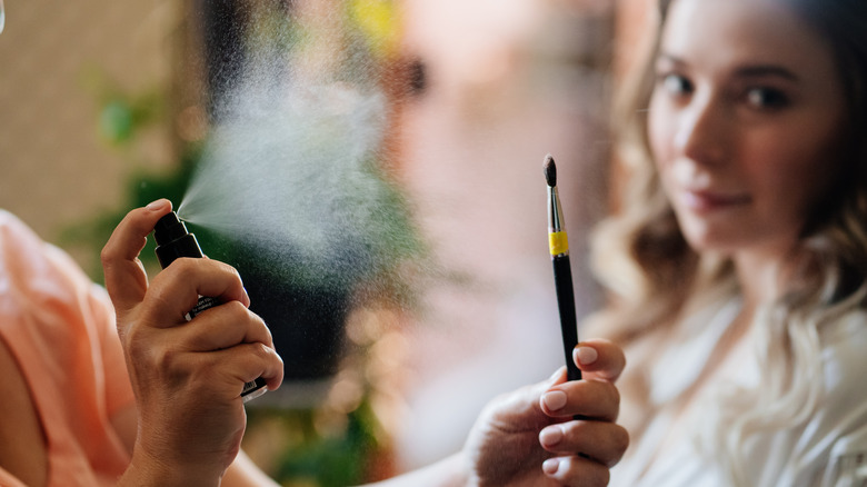 A makeup artist spraying setting spray on a brush