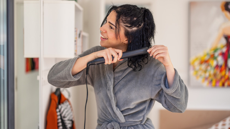 A woman straightening her hair in a bathrobe