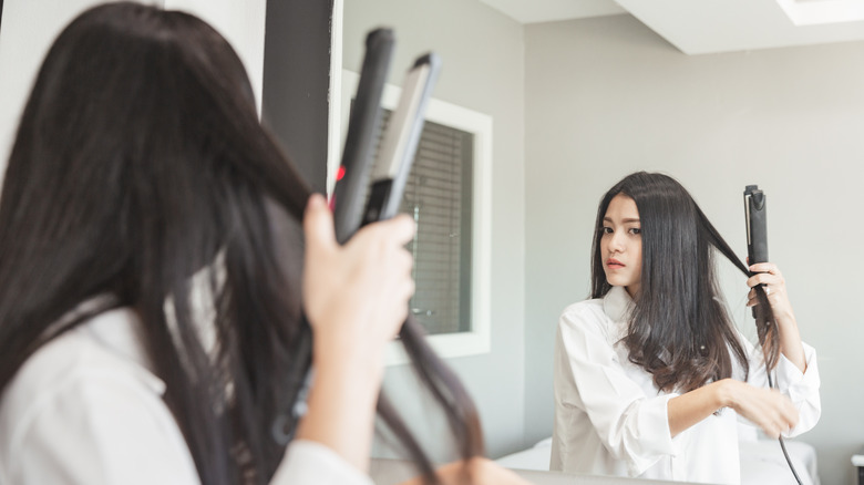 A woman straightening her hair in a mirror