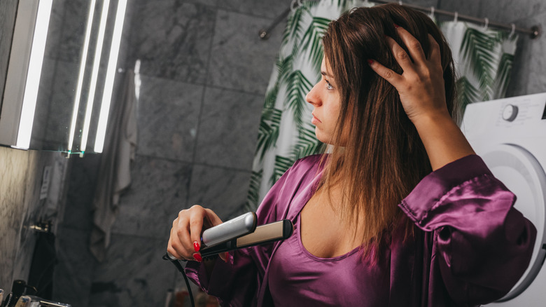 A woman straightening her hair and looking in the mirror