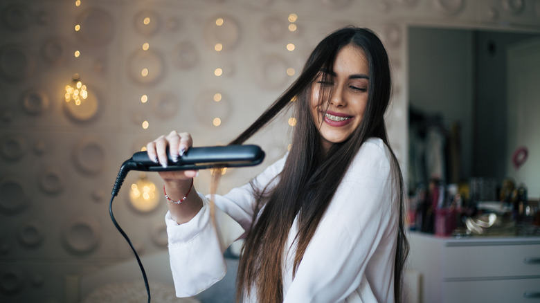 A woman smiling and straightening her long hair