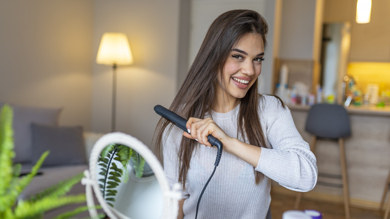 A smiling woman straightening her hair