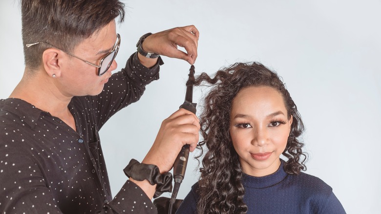 Hairstylist curling woman's hair