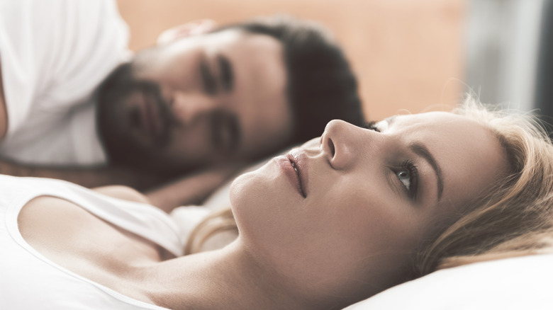 woman pondering in bed while man sleeps