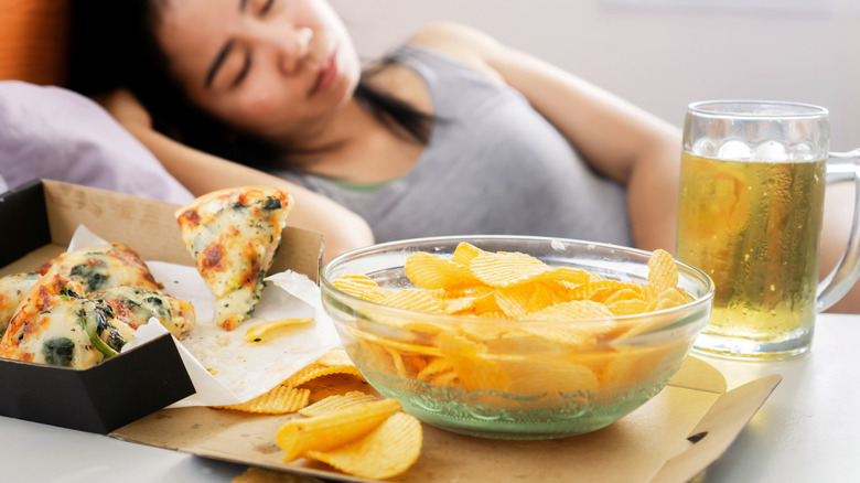 Woman sleeping by pizza and chips 