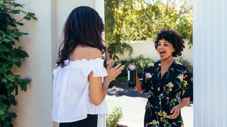 smiling woman gifts hostess with a wine bottle