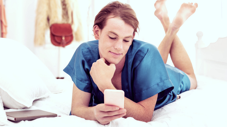 Trans person lies in bed looking at phone