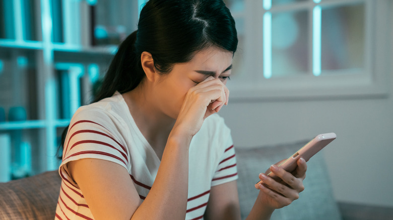 Woman rubbing eyes on phone 