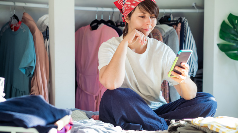 woman on her phone surrounded by clothes on her bed