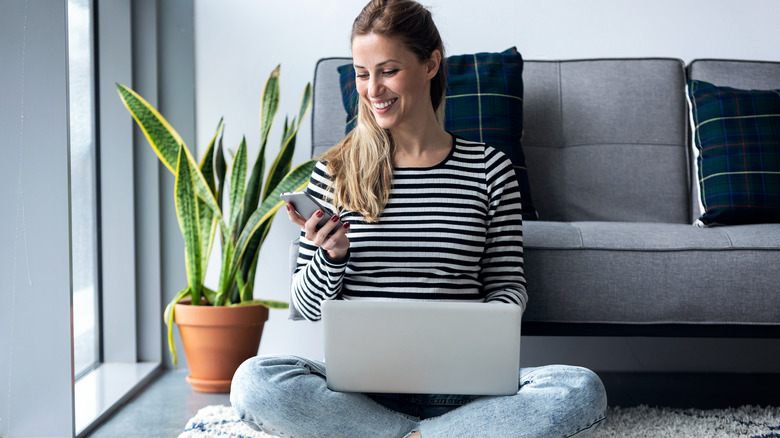 woman on her phone and her computer sitting on the floor