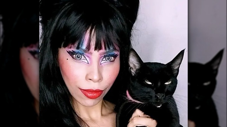 Woman wearing Elvira makeup holding cat