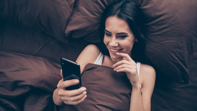 smiling woman in bed with phone