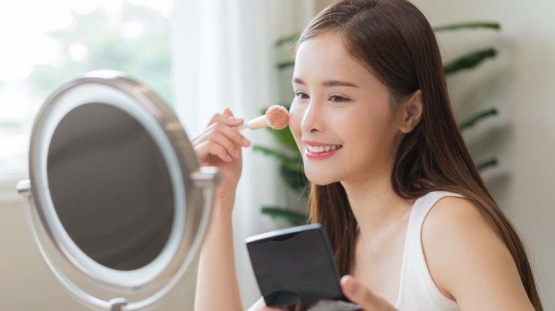 Woman looking in the mirror and smiling while applying blush