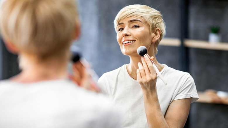 Woman with short blond hair applying makeup with a large brush