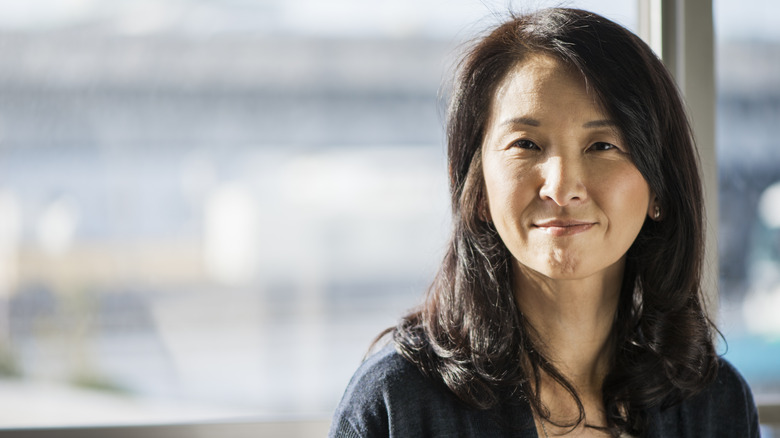 A woman with shoulder-length layered hair looking content as she stares at the camera in front of a window.