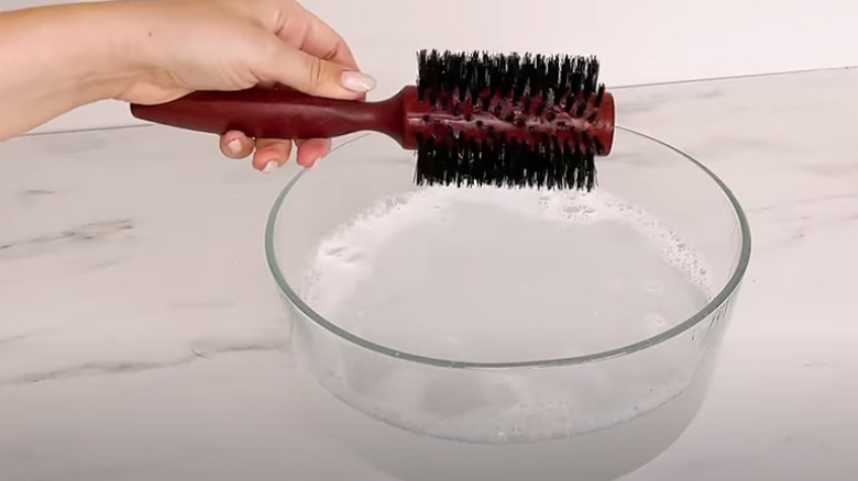 A person washing a hairbrush in a bowl of water.