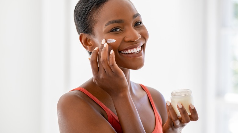 Smiling woman applying moisturizer on cheek