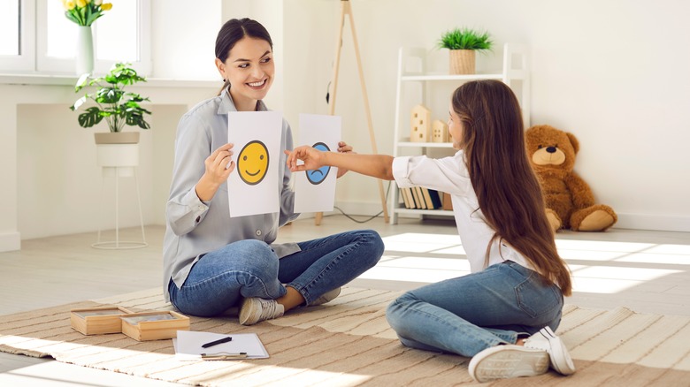 woman holds up smiley and sad face to child