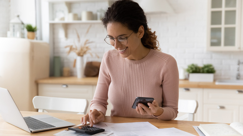 woman smiling using calculator and laptop