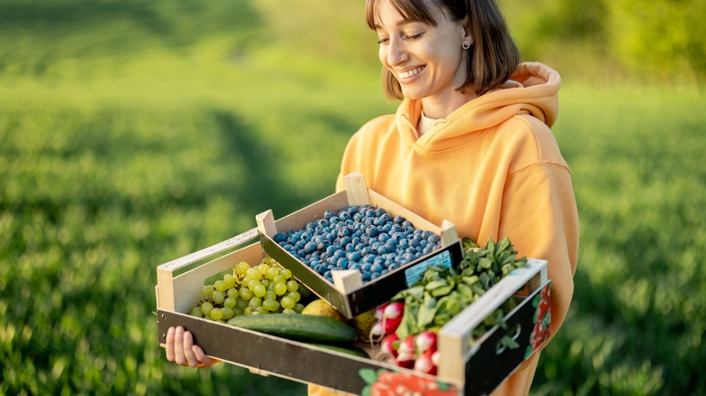 smiling woman carrying boxes of fruit and vegetables