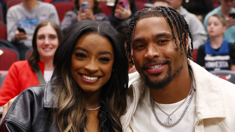 Simone Biles and Jonathan Owens smiling at a basketball game.