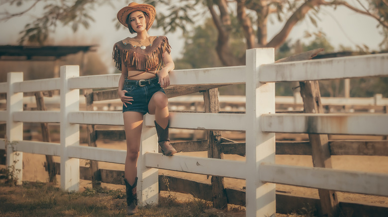 Cowgirl leaning on white fence