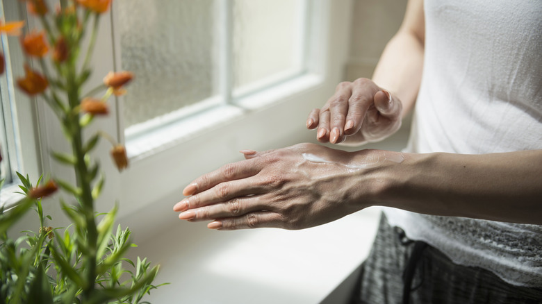 Woman applying SPF to her hands by the window