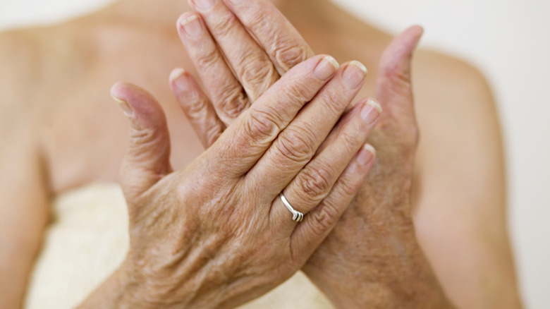 An older woman holds her hands out while standing in a bath towel