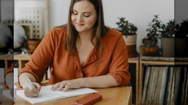 A woman writing in a notebook at a table.