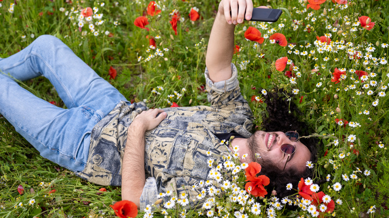 A man taking a selfie while lying among flowers