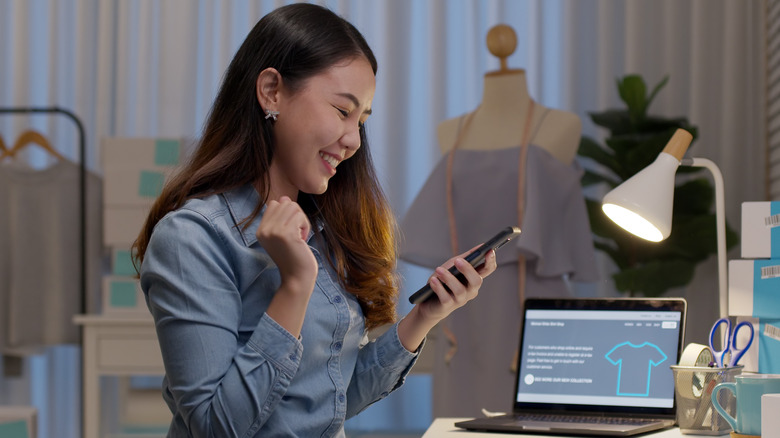 Woman making transaction on phone next to laptop