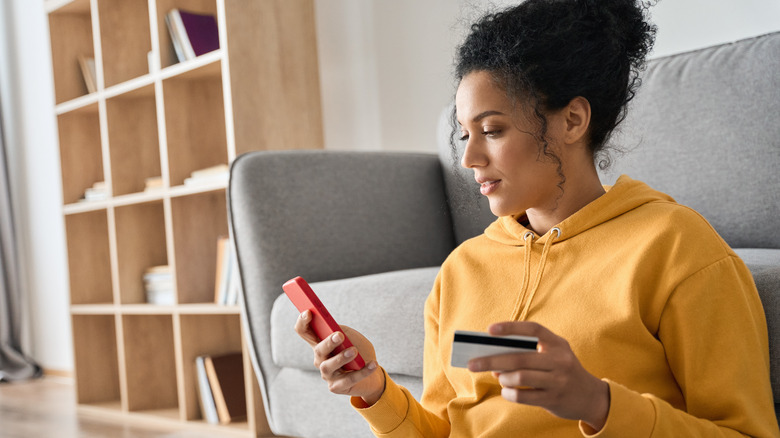 Woman glancing at cell phone while holding credit card