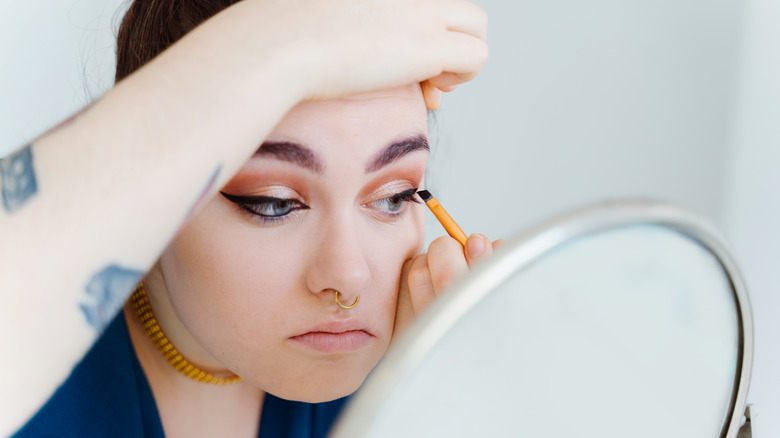 A woman looking in the mirror and applying winged eyeliner with a brush